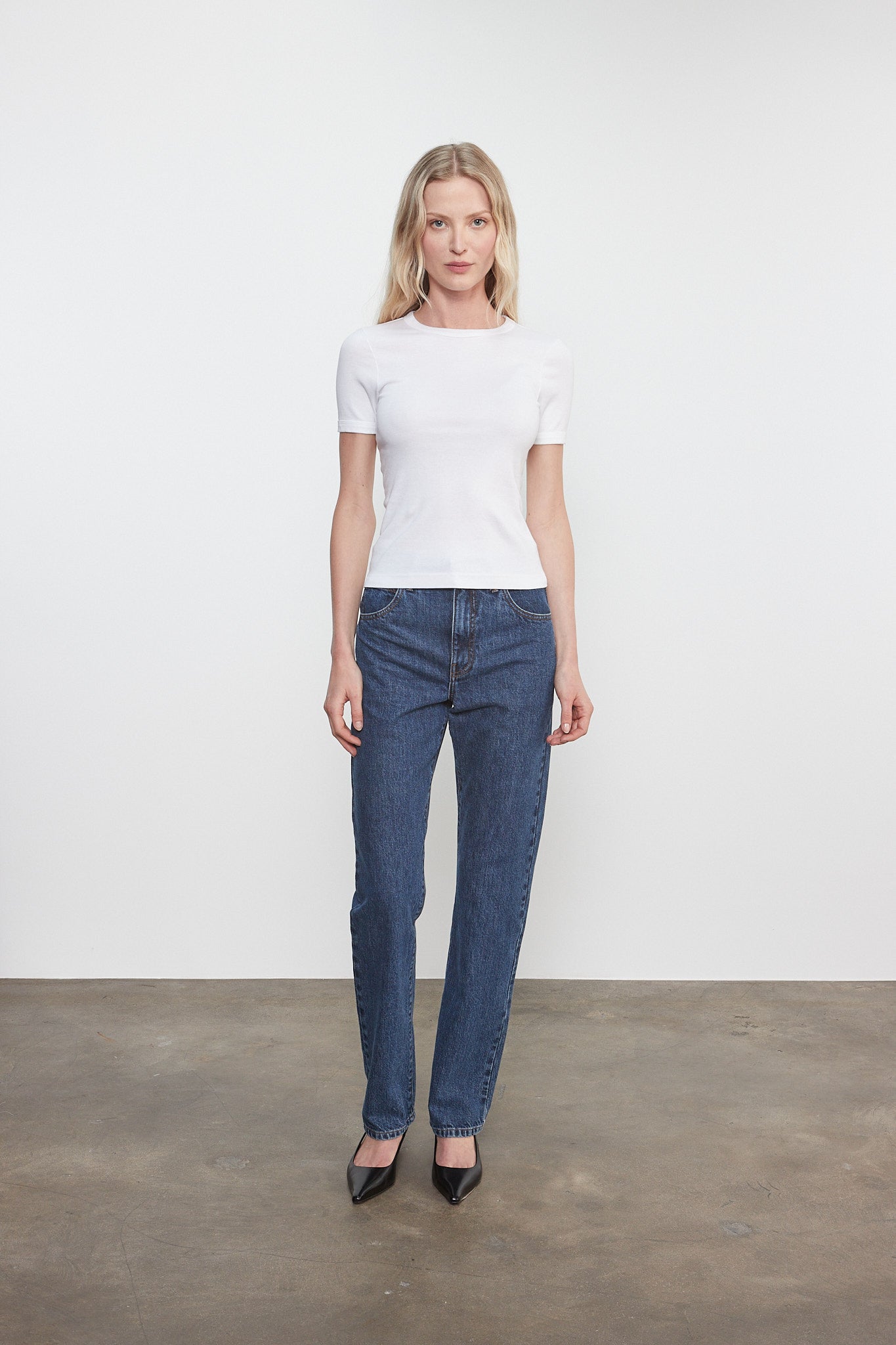 Woman wearing a white t-shirt and blue jeans standing against a plain white background