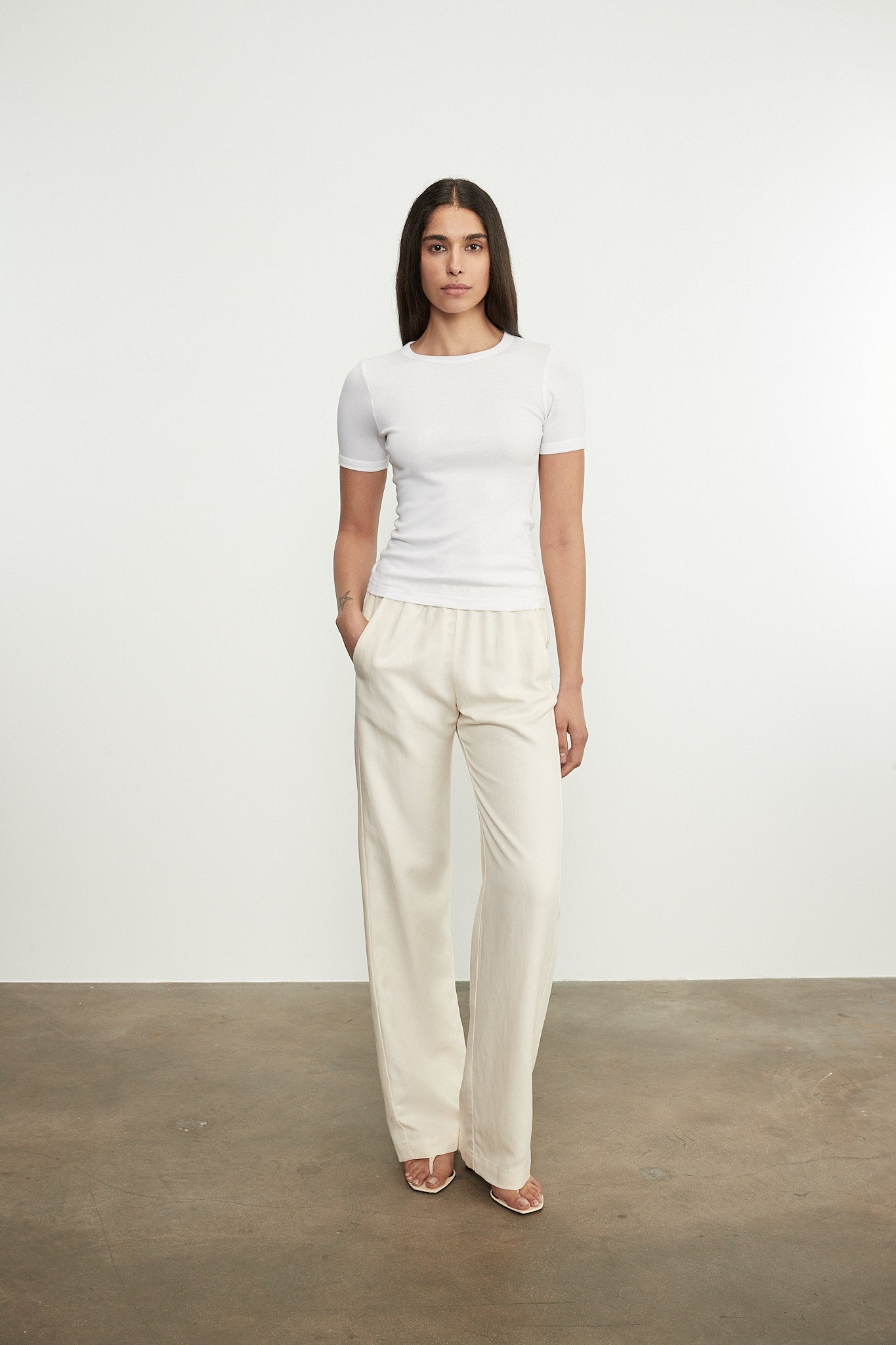 Woman wearing a white top and beige pants against a plain background