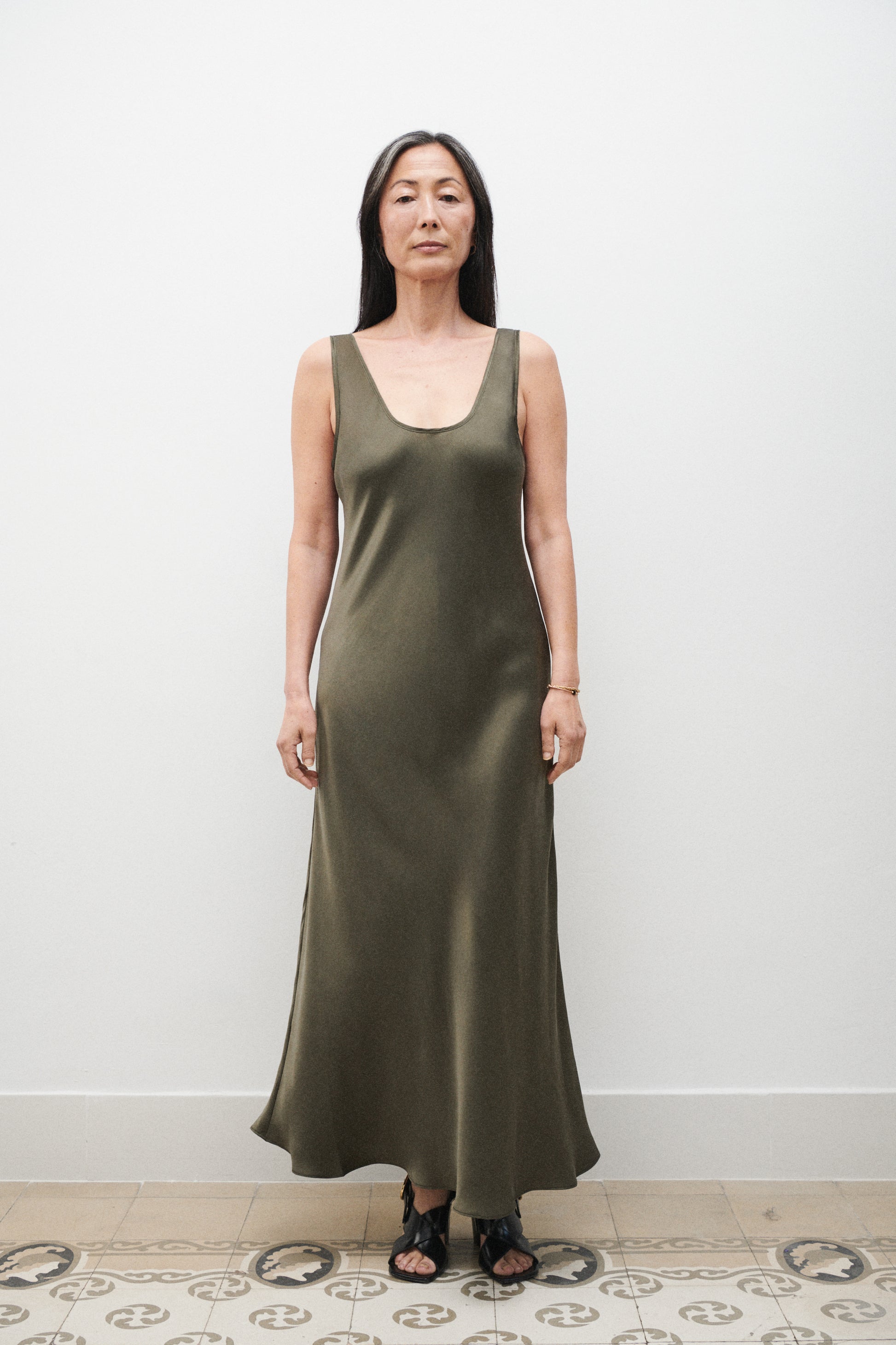 Woman wearing a green dress standing against a white wall.