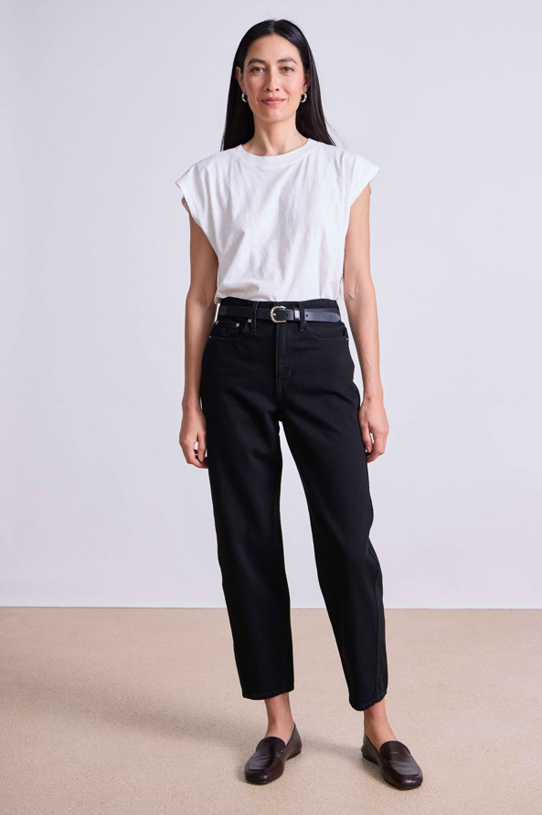 Woman wearing a white top and black pants against a plain background