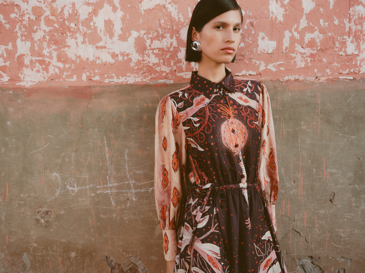 Woman wearing a patterned dress standing against a textured wall.