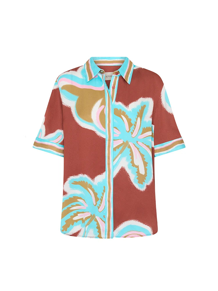 A short-sleeve button-up shirt with a brown base and a colorful tropical palm leaf pattern in light blue, beige, and pink, displayed on a clean white background.