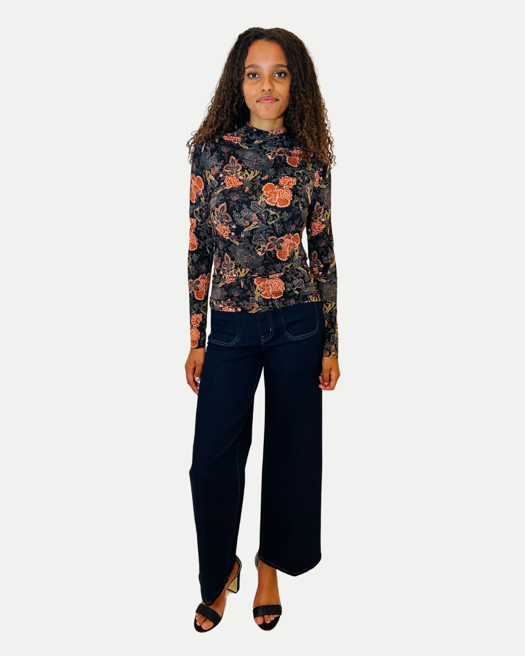 Woman wearing a floral blouse and dark jeans on a white background