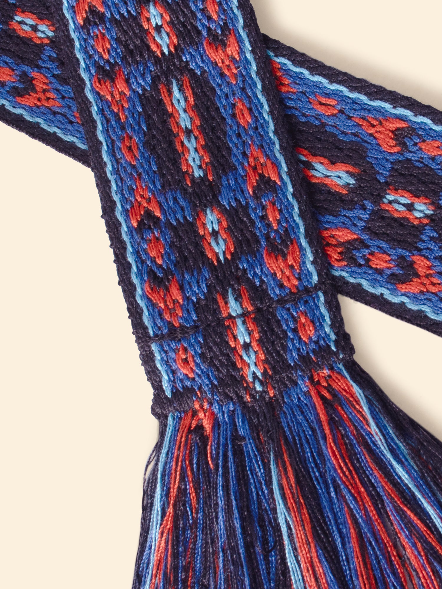 Close-up of a blue and red woven strap with intricate patterns on a beige background