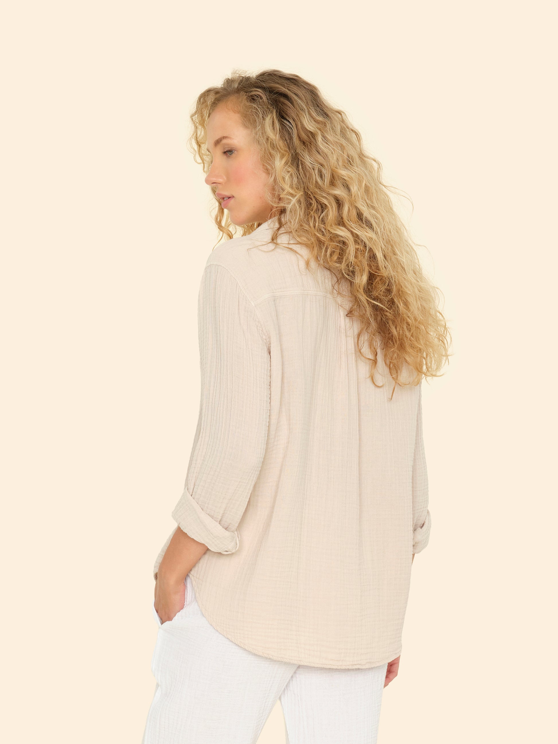 Woman wearing a beige sweater and white pants on a light beige background