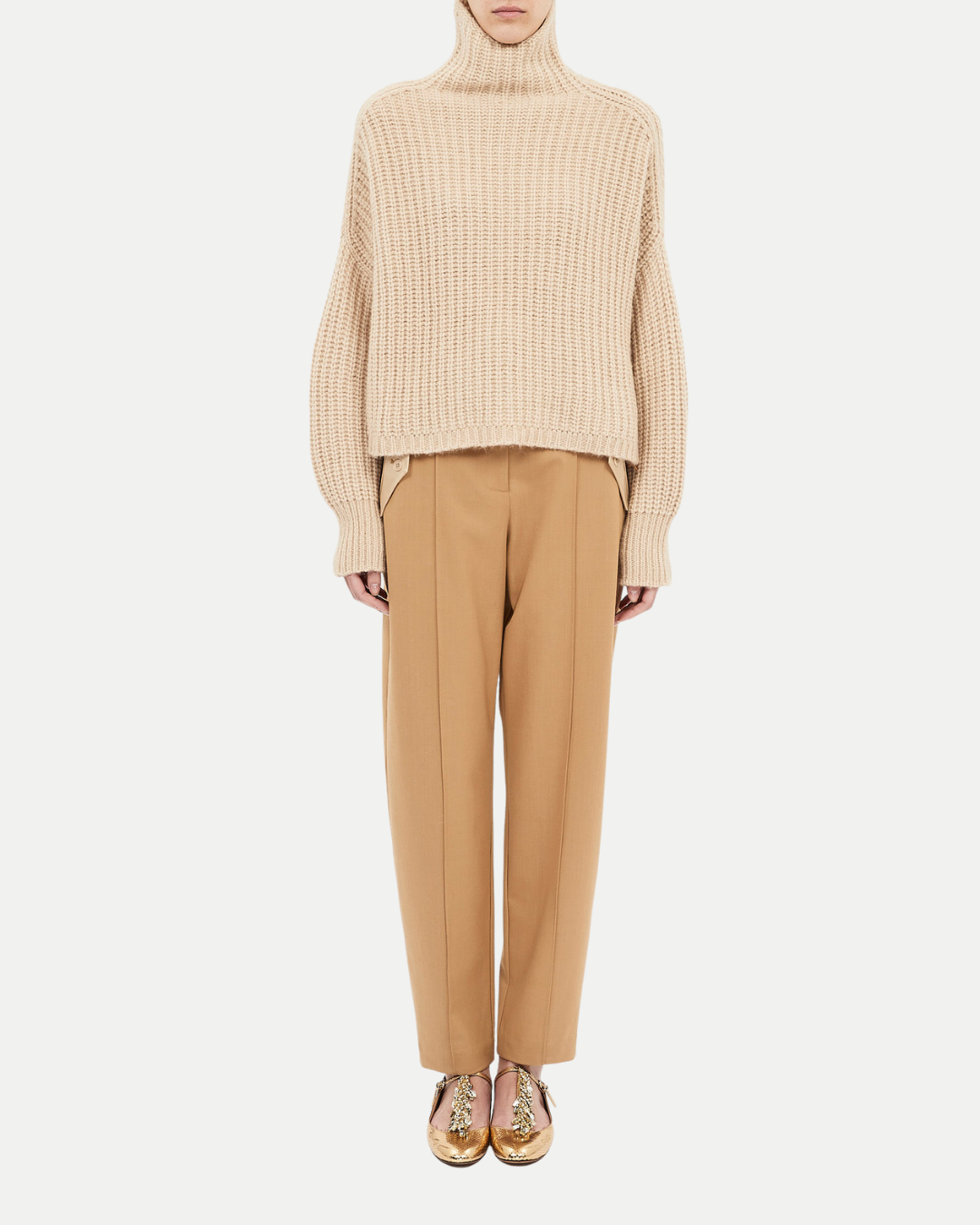 Person wearing a beige ribbed sweater and tan pants on a white background