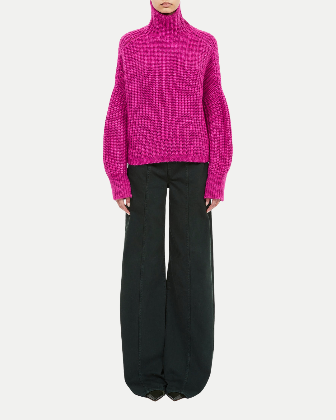 Person wearing a bright pink sweater and black pants on a white background