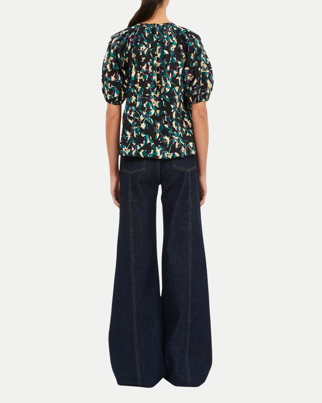 Person wearing a patterned top and dark jeans on a white background