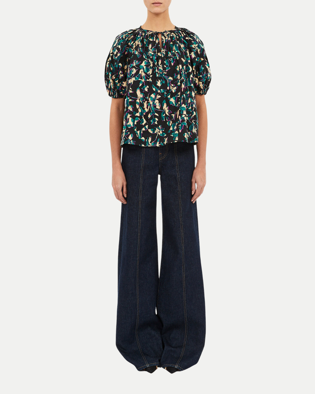 Person wearing a patterned top and dark jeans on a white background