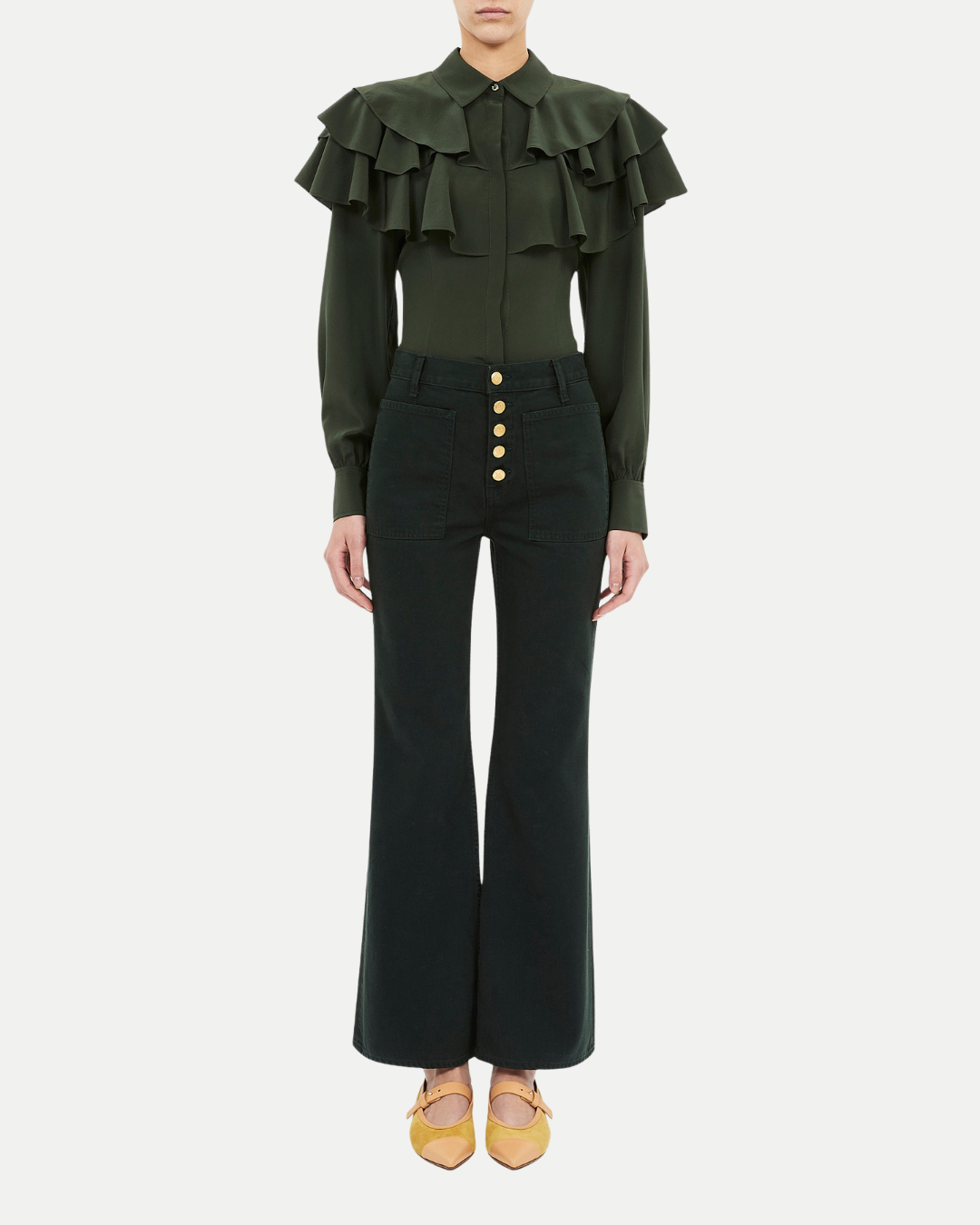 Person wearing a green ruffled blouse and black high-waisted pants on a white background