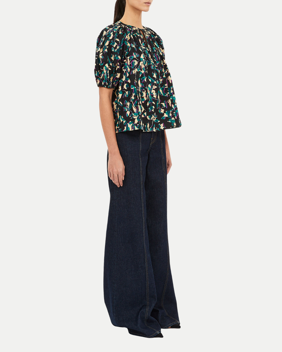 Woman wearing a patterned top and dark pants on a white background