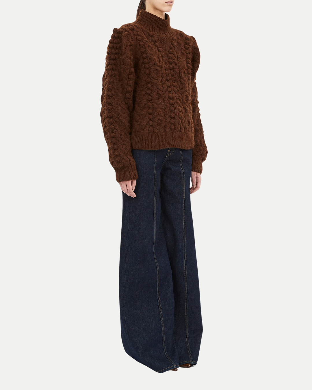 Person wearing a brown knitted sweater and dark blue jeans on a white background