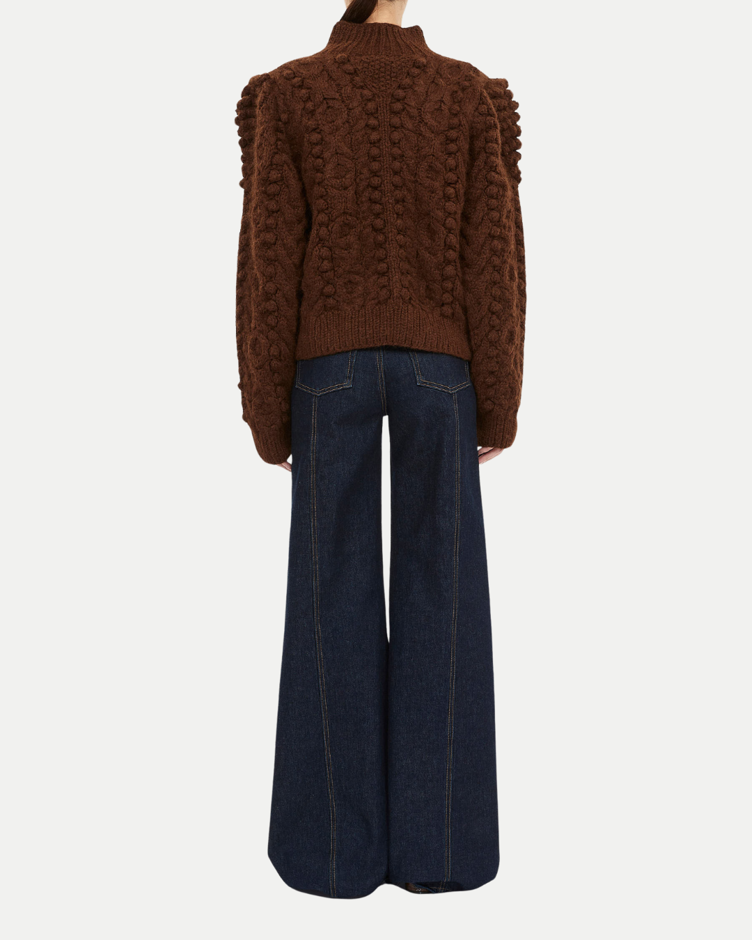 Brown cable knit sweater and dark blue jeans on a white background