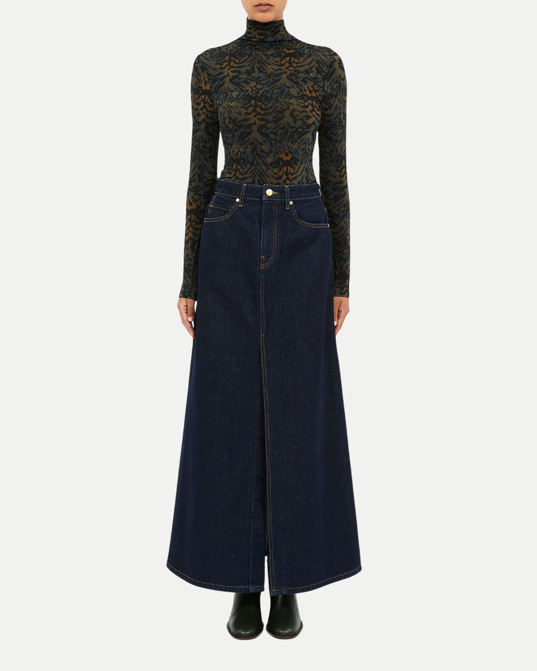 Person wearing a long dark denim skirt with a fitted black turtleneck top on a white background