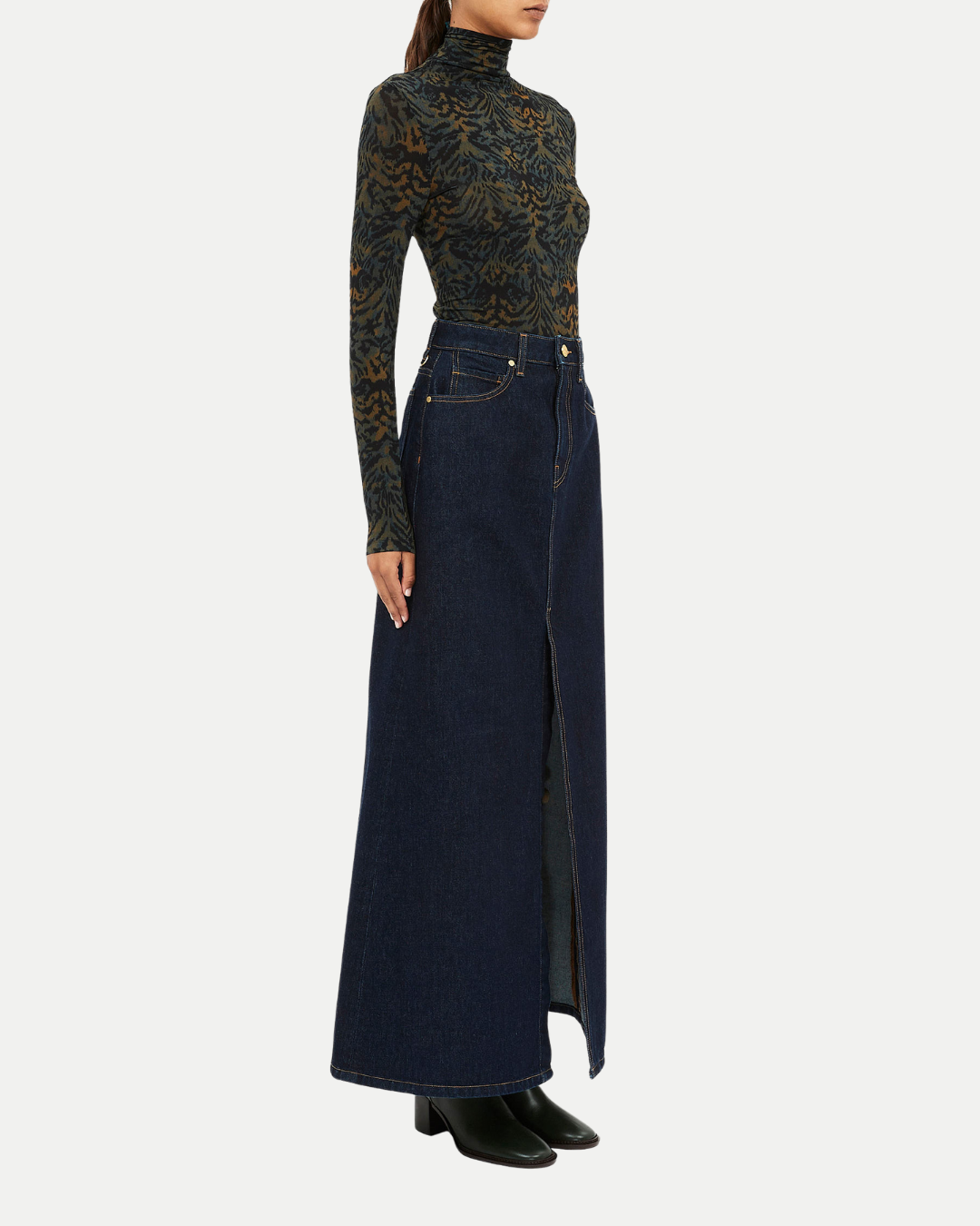 Person wearing a patterned long-sleeve top and dark denim skirt on a white background