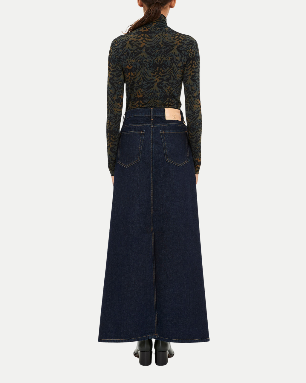 Person wearing a long dark denim skirt with a patterned top on a white background