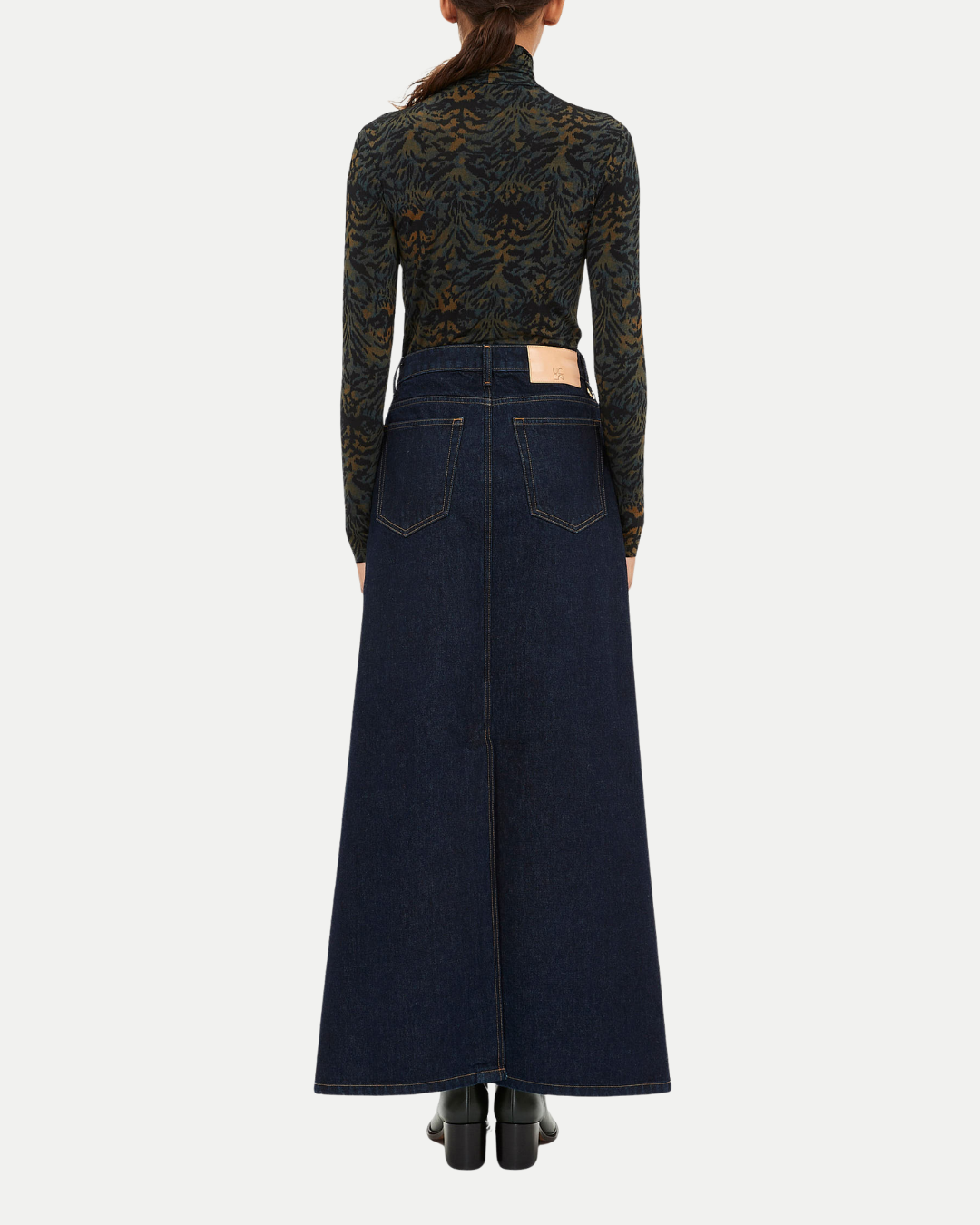 Person wearing a long dark denim skirt with a patterned top on a white background
