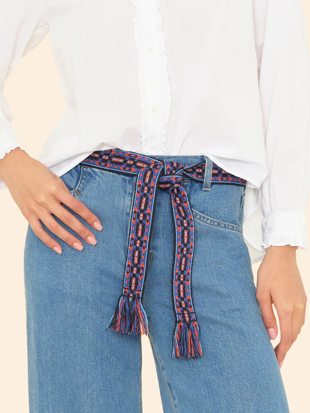 Person wearing blue jeans with a patterned belt on a beige background