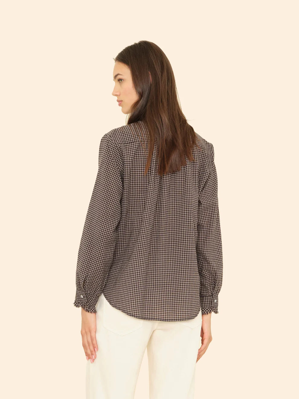 Woman wearing a checkered shirt and white pants on a beige background