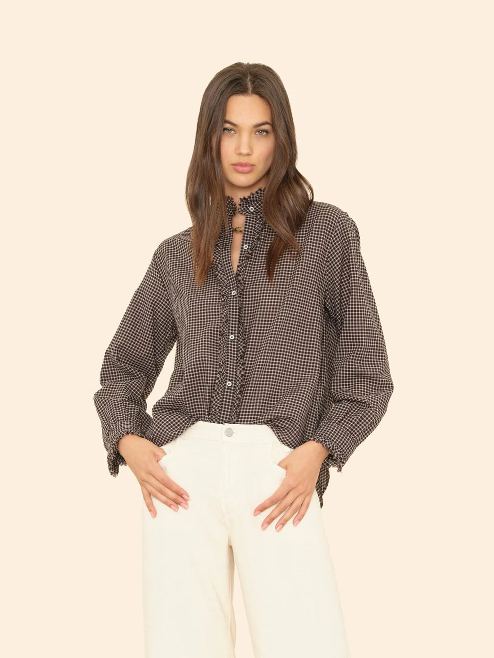 Woman wearing a patterned blouse and white pants on a beige background