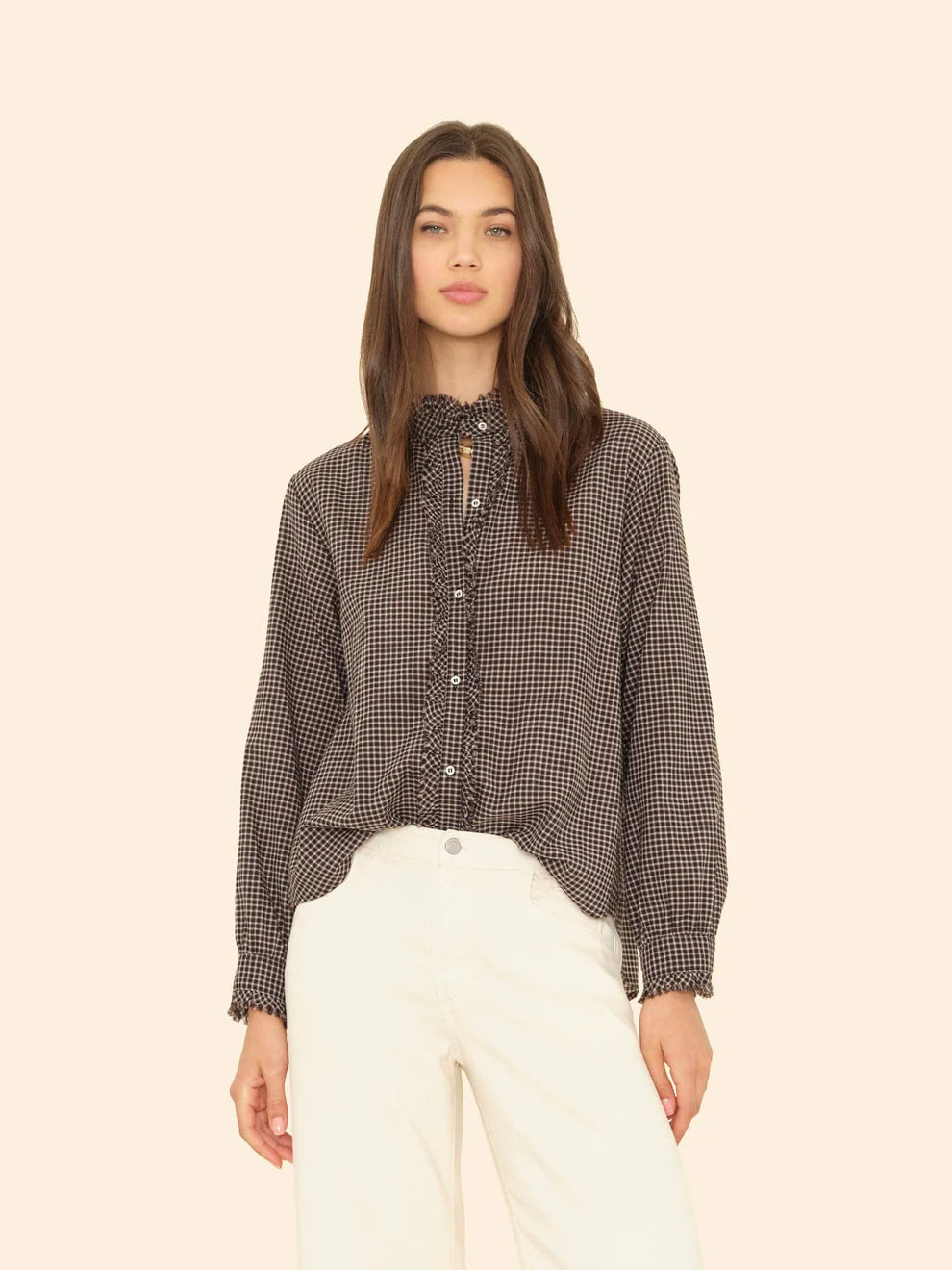Woman wearing a checkered blouse and white pants on a beige background