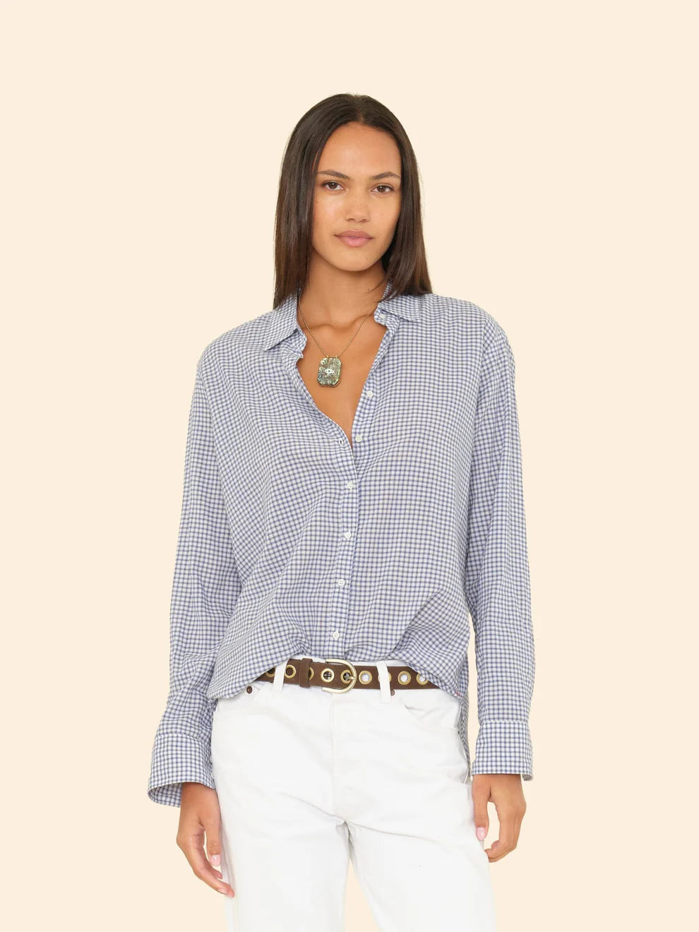 Woman wearing a blue checkered shirt and white pants on a beige background