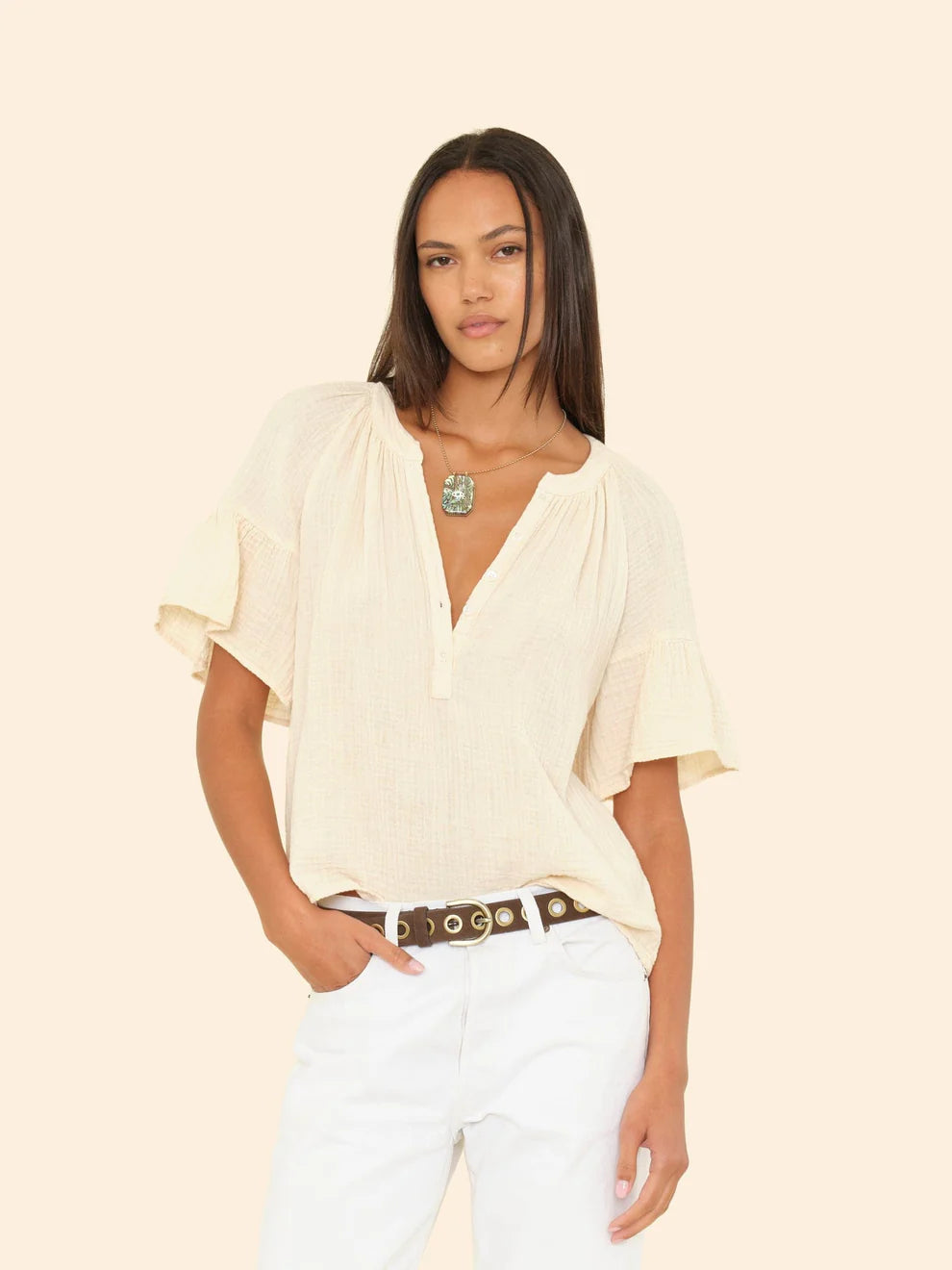 Woman wearing a light-colored blouse and white pants on a beige background